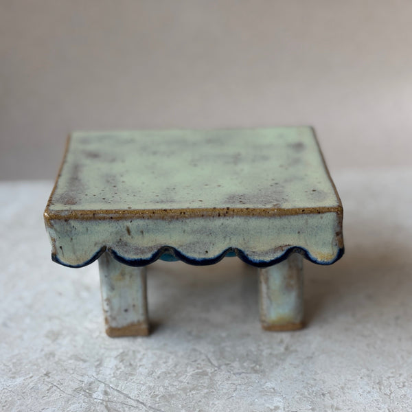 Small ceramic table with a scalloped edge on a light gray surface