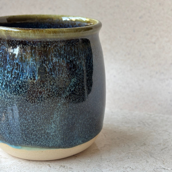 Ceramic cup with blue speckled glaze on a light gray background