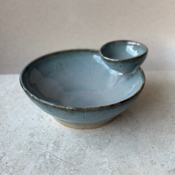 Blue ceramic cherry bowl with pit catcher on a light gray surface
