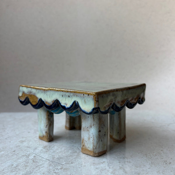 Small ceramic table with wavy edge on a white surface